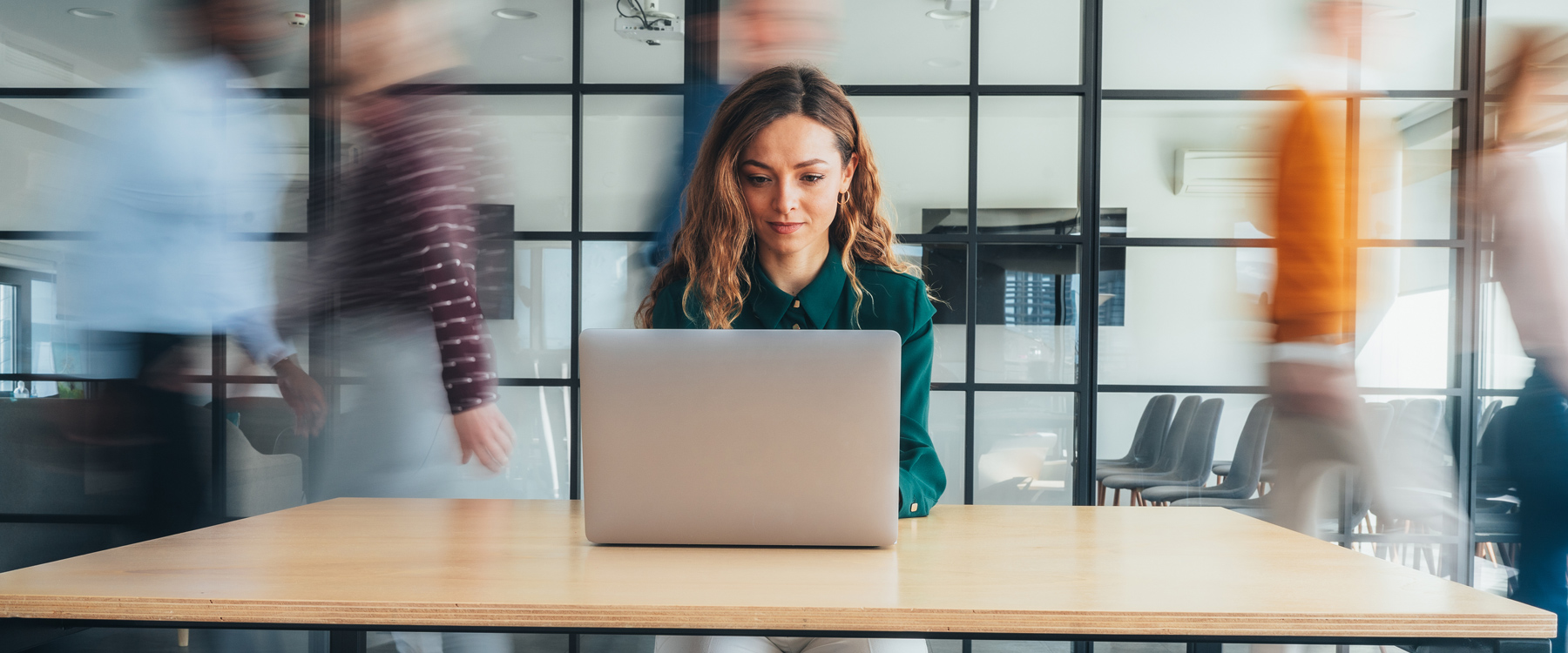 woman working on laptop with blurred images of people walking behind her