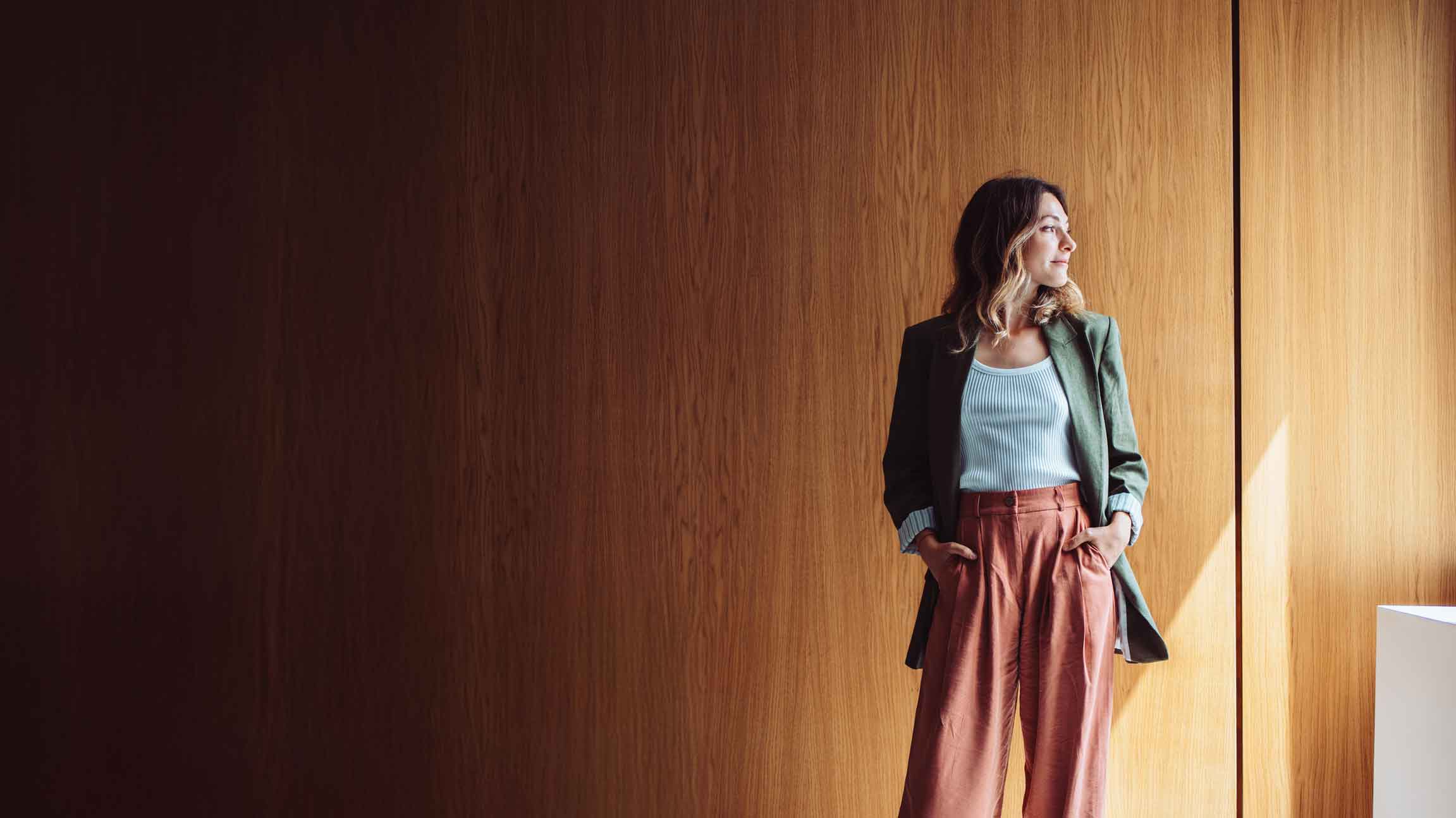 businesswoman in green jacket standing in front of large paneled office wall