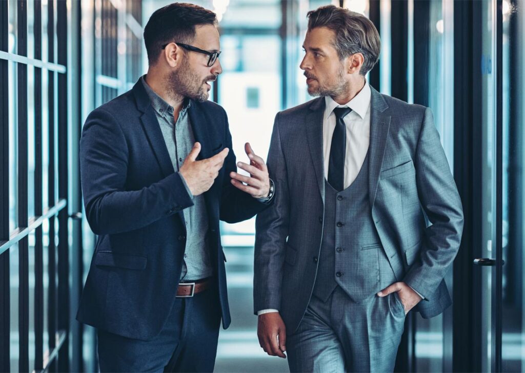 two businessmen talking while wlaking down the office hallway